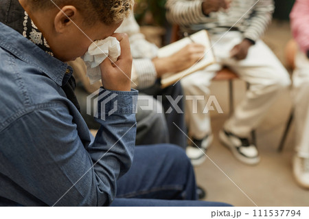 Side view portrait of person crying during emotional therapy session and wiping tears with tissue, copy space 111537794
