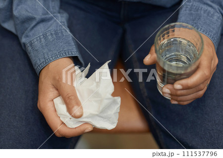 Top view closeup of unrecognizable person holding tissue and glass of water during emotional therapy session, copy space 111537796
