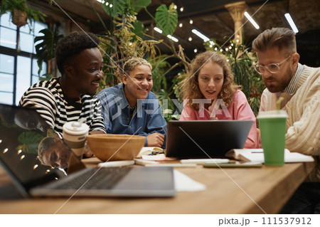Diverse young business team looking at computer screen reviewing data during meeting in green coworking space 111537912