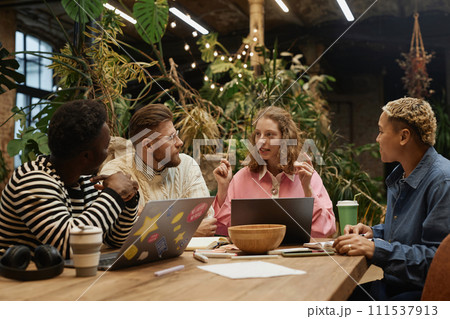 Portrait of young businesswoman wearing pink while leading business meeting with diverse team in green office 111537913