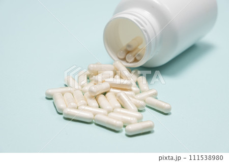 White medicine capsules spilled out of a jar on light blue background close-up. 111538980