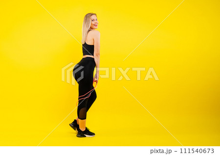 Fitness woman doing jumping exercises with skipping rope on colorful yellow red background. 111540673