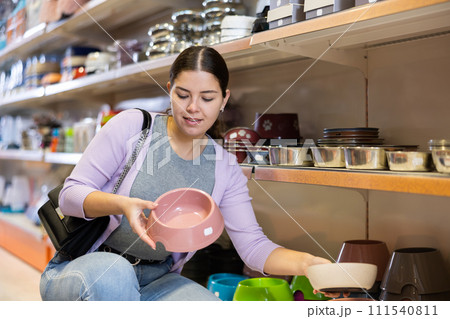 Young woman choosing bowl for puppy in pet supplies store 111540811