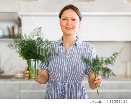 Satisfied woman with dill in her hands in kitchen 111541112