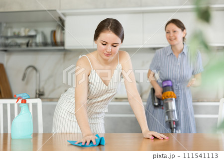 Young girl cleaning the table surface, mother vacuum-cleaning in the kitchen 111541113