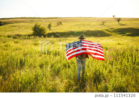 4th of July. American Flag. Traveler with the flag of America. The man in a hat, a backpack, a shirt and jeans. 4th of July. American Flag. Traveler with the flag of America. The man in a hat, a backpack, a shirt and jeans. 111541320