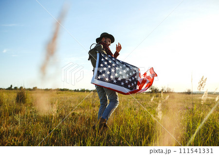 4th of July. American Flag. Traveler with the flag of America. The man in a hat, a backpack, a shirt and jeans. 111541331