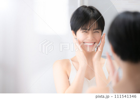 美容などのイメージで使いやすい洗面台で鏡を見る美しい女性 両手で頬を 左にコピースペース 美容などのイメージで使いやすい洗面台で鏡を見る美しい女性 両手で頬を 左にコピースペース 111541346