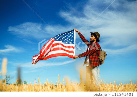 4th of July. American Flag. Traveler with the flag of America. The man in a hat, a backpack, a shirt and jeans. 111541401