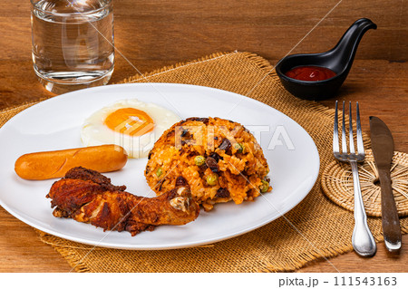 American fried rice with fried drumstick, fried egg and sausage in white ceramic plate. American fried rice with fried drumstick, fried egg and sausage in white ceramic plate. 111543163