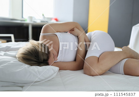 Woman at home lying on bed with stomach pain 111545837