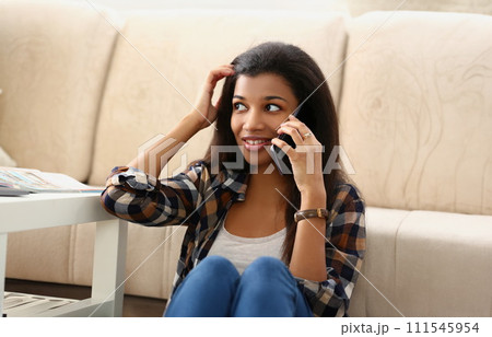 A dark-skinned girl on the floor house speaks on a phone 111545954