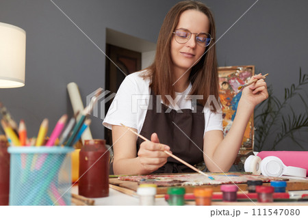 Artistic talent workshop. Painter's creative studio. Artwork inspiration session. Caucasian woman painter wearing brown apron in art studio drawing picture Artistic talent workshop. Painter's creative studio. Artwork inspiration session. Caucasian woman painter wearing brown apron in art studio drawing picture 111547080