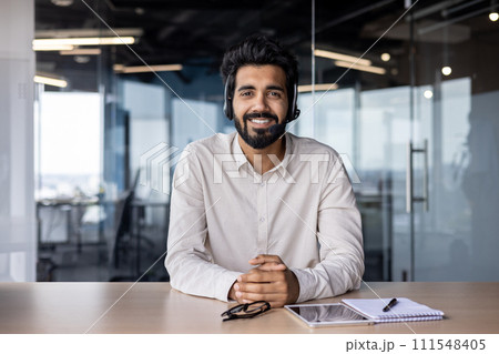 Portrait of a smiling Muslim man businessman, marketer, salesman sitting in the office at the table in a headset and smiling confidently at the camera. 111548405