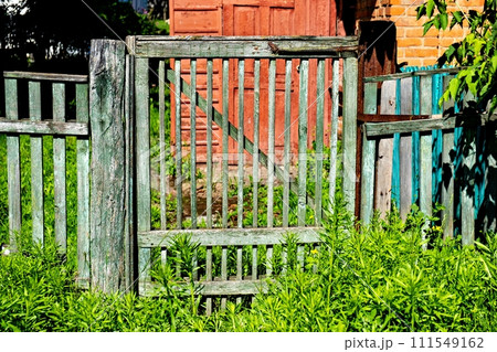 Green wooden gate in front of red door and window. 111549162