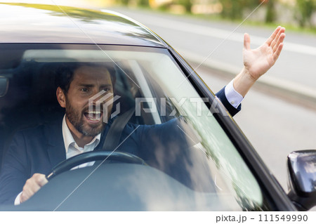 Close-up photo of an angry young businessman driving a car, shouting and waving his hands. 111549990