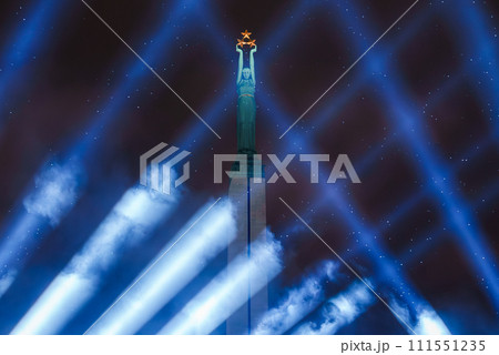 An illuminated Freedom Monument reaches into the night sky in Riga, Latvia, with beams of light converging at its base and a figure holding stars aloft, celebrating Independence Day. An illuminated Freedom Monument reaches into the night sky in Riga, Latvia, with beams of light converging at its base and a figure holding stars aloft, celebrating Independence Day. 111551235