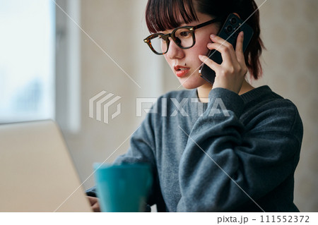 パソコンをタイピングしながら電話をする若い女性 111552372