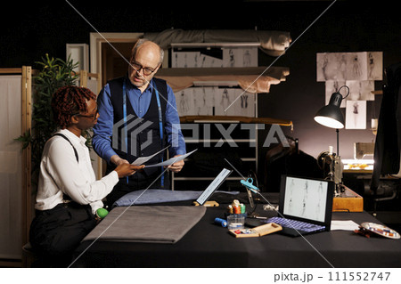 African american needleworker apprentice helping master couturier pick best sartorial outfit design for runway show collection. Tailor and assistant brainstorming ideas for creative bespoken attire 111552747