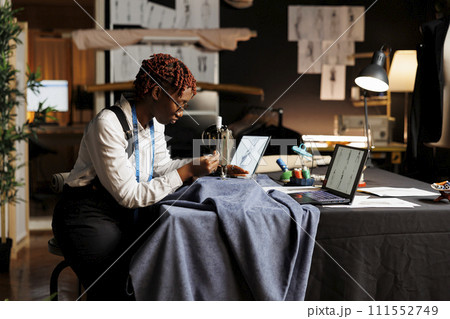 Seamstress using industrial sewing machine to do creative embroidery on garment for upcoming handmade clothing. Suitmaker working on sartorial bespoken designs in atelier shop workshop 111552749
