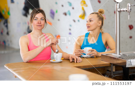 Two sportive women drinking coffee and talking in climbing center Two sportive women drinking coffee and talking in climbing center 111553197
