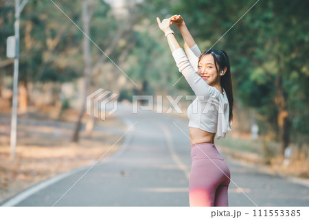 Fitness concept, Cheerful young woman in sportswear stretching arms while enjoying a workout in a peaceful park setting. 111553385