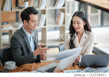 Two business workers smiling happy working sitting on desk at the office. Two business workers smiling happy working sitting on desk at the office. 111556911