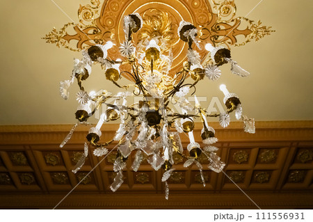 Crystal gold chandelier or luster with long electric candles on stucco ceiling. View from below 111556931