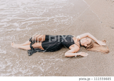 Woman summer travel sea. Happy tourist in black dress enjoy taking picture outdoors for memories. Woman traveler posing on sea beach surrounded by volcanic mountains, sharing travel adventure journey Woman summer travel sea. Happy tourist in black dress enjoy taking picture outdoors for memories. Woman traveler posing on sea beach surrounded by volcanic mountains, sharing travel adventure journey 111559885