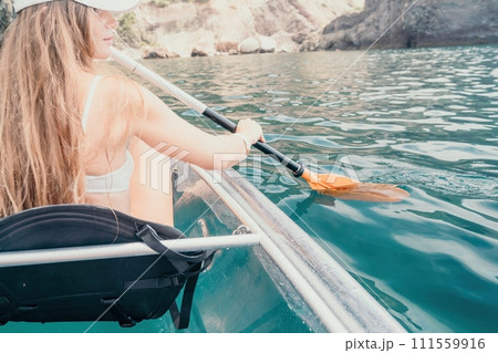 Woman in kayak back view. Happy young woman with long hair floating in transparent kayak on the crystal clear sea. Summer holiday vacation and cheerful female people relaxing having fun on the boat 111559916