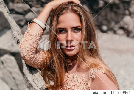 Woman summer travel sea. Happy tourist in beige dress enjoy taking picture outdoors for memories. Woman traveler posing on the beach surrounded by volcanic mountains, sharing travel adventure journey 111559966