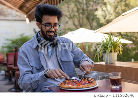 Man sitting at the table in a cafe cutting pizza Man sitting at the table in a cafe cutting pizza 111562646