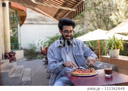 Man sitting at the table in a cafe cutting pizza Man sitting at the table in a cafe cutting pizza 111562648