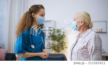 Nurse and senior patient in protective face masks greeting each other 111563421