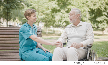Hospital therapist supporting elderly pensioner in wheelchair, communication 111564364
