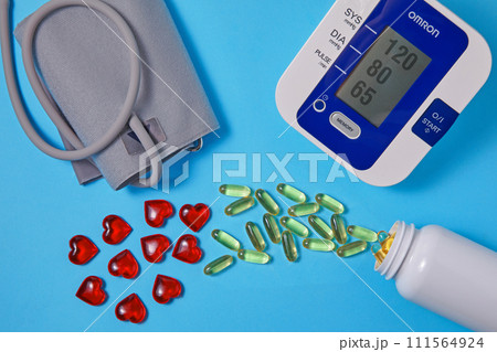 Omega-3 polyunsaturated fatty acids and red hearts pour out from a white plastic jar and a blood pressure monitor on a blue background. Prevention and treatment of atherosclerosis and hypertension Omega-3 polyunsaturated fatty acids and red hearts pour out from a white plastic jar and a blood pressure monitor on a blue background. Prevention and treatment of atherosclerosis and hypertension 111564924