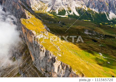 Observation point overlooking bare peak of Seceda mountain in white dense fog. Rocky ridgeline with grassy slopes in Alps aerial view 111565720
