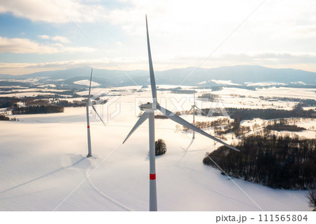 Panoramic view of wind generators in a winter field at dusk. Production of green energy. Panoramic view of wind generators in a winter field at dusk. Production of green energy. 111565804