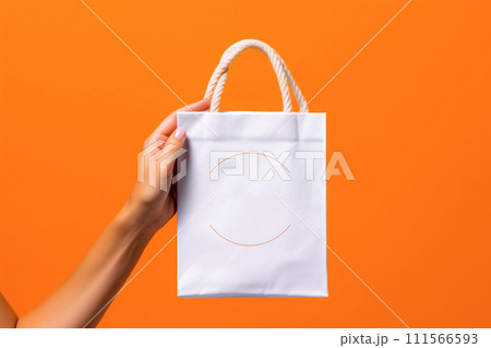 Woman's hand holding white paper shopping bag on orange background. Shopping concept. 111566593
