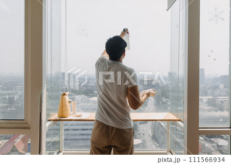 Backside view of asian Thai man wiping window glass in room apartment with city view, keep glass sparking clean, housework concept. Backside view of asian Thai man wiping window glass in room apartment with city view, keep glass sparking clean, housework concept. 111566934