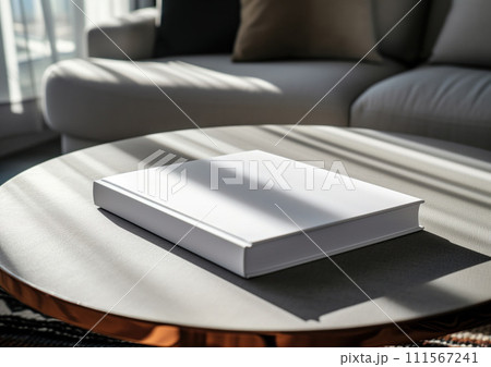 Advertising close up mockup shot of book lying on white coffee table with white sofa and sun rays at the background 111567241