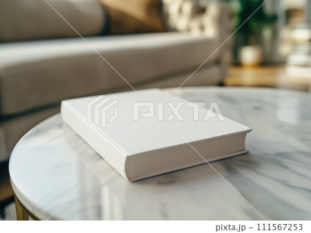 Advertising close up mockup shot of book lying on white marble coffee table with white sofa and sun rays at the background Advertising close up mockup shot of book lying on white marble coffee table with white sofa and sun rays at the background 111567253