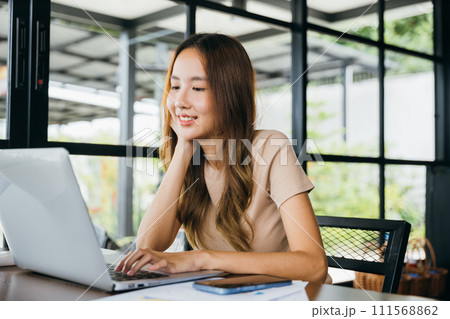 Happy businesswoman smiling sitting alone at cafe desk with laptop computer she looking out of window, portrait of beautiful woman smile in coffee shop in morning, freelance lifestyle Happy businesswoman smiling sitting alone at cafe desk with laptop computer she looking out of window, portrait of beautiful woman smile in coffee shop in morning, freelance lifestyle 111568862
