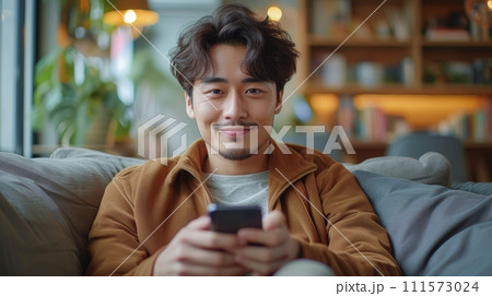 AI-generated content. A handsome Asian man uses his smartphone in the living room, leaning on the couch while browsing the internet or messaging friends, enjoying weekend at home. 111573024