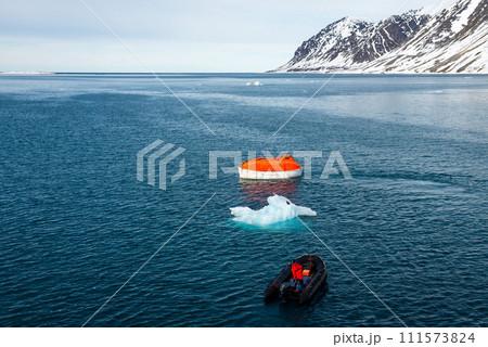 Maneuvering orange lifeboat in water in Arctic waters, Svalbard. Abandon ship drill. Lifeboat training. Man over board drill. Maneuvering orange lifeboat in water in Arctic waters, Svalbard. Abandon ship drill. Lifeboat training. Man over board drill. 111573824