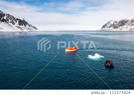 Maneuvering orange lifeboat in water in Arctic waters, Svalbard. Abandon ship drill. Lifeboat training. Man over board drill. Maneuvering orange lifeboat in water in Arctic waters, Svalbard. Abandon ship drill. Lifeboat training. Man over board drill. 111573826