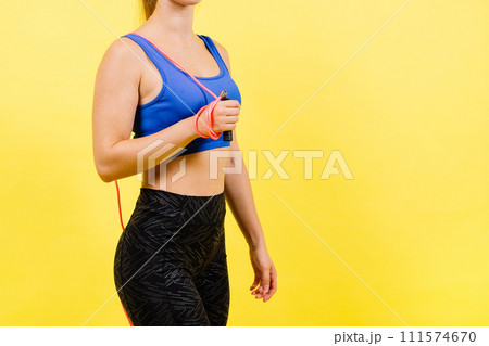 Portrait of gentle muscular woman holding skipping rope on her neck isolated over yellow background 111574670