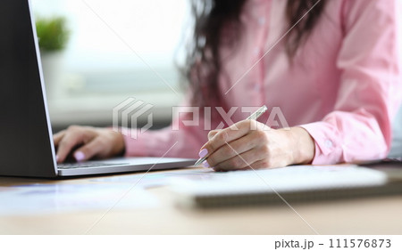 Woman makes notes with pen on sheet and on laptop Woman makes notes with pen on sheet and on laptop 111576873