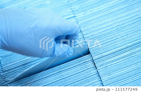 Doctor hand in rubber gloves pulling out sterile disposable napkin from packaging closeup Doctor hand in rubber gloves pulling out sterile disposable napkin from packaging closeup 111577249