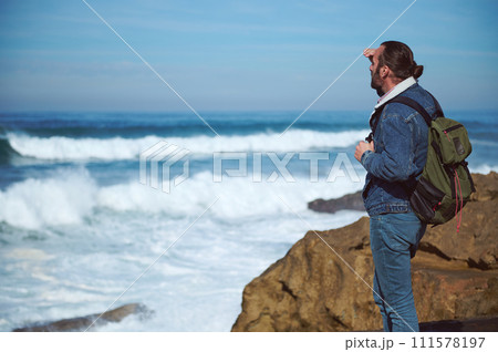 Absorbed bearded young male adventurer standing on a cliff and looking at horizon, enjoying the view of beautiful nature Absorbed bearded young male adventurer standing on a cliff and looking at horizon, enjoying the view of beautiful nature 111578197